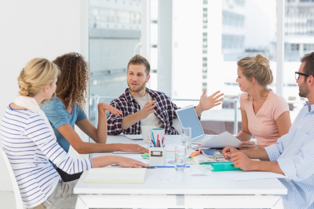 Five adults discussing ideas around a table with a laptop and papers.